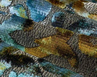 May include: A textured fabric featuring a dense pile with an abstract pattern in shades of deep teal, mustard yellow, and metallic silver. The material displays a multi-layered appearance with raised velvet-like sections and woven base.
