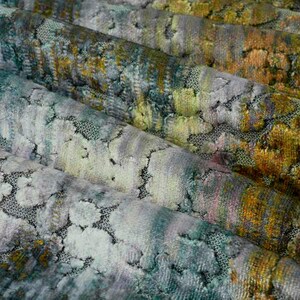 May include: Close-up of a textured fabric with a green, blue, and yellow color scheme. The fabric has a subtle shimmer and a slightly raised pattern.
