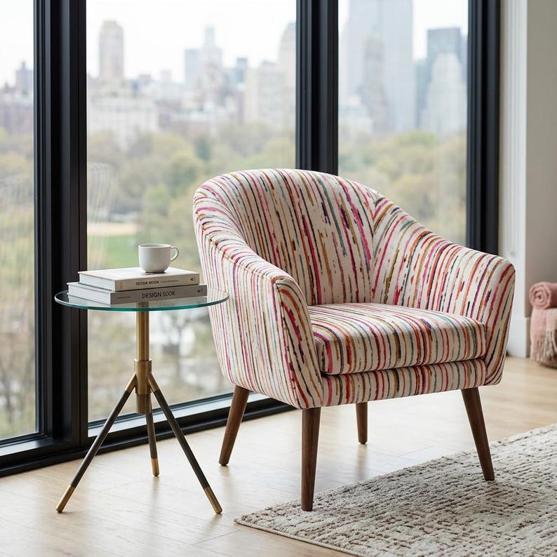 May include: An upholstered barrel chair with a multi-colored vertical stripe pattern in shades of pink, orange, and blue on a cream background, featuring dark wooden legs, positioned next to a round glass side table with a brass and black metal base.