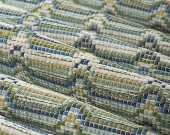 May include: A woven fabric featuring a repeating geometric pattern in shades of blue, green, and white. The textile has a textured, multi-dimensional surface with visible interlaced threads forming a structured grid and wave-like design.