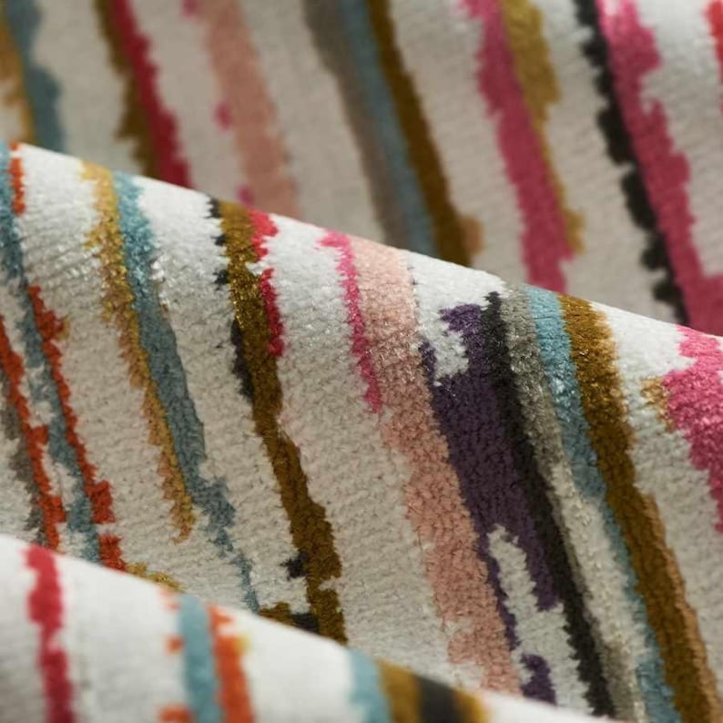 May include: A textured fabric featuring a repeating pattern of vertical stripes in various colors including pink, blue, gold, orange, and dark purple against an off-white background. The material has a soft, slightly raised pile surface.