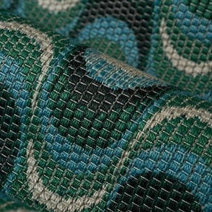 May include: Close-up of a woven fabric with a repeating pattern of blue, green, and white circles. The fabric has a textured surface and a slightly iridescent sheen.