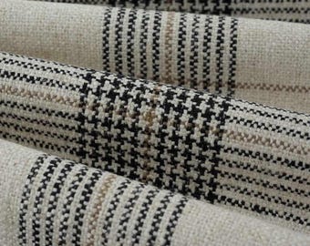 May include: A woven fabric featuring a textured, off-white base with a repeating plaid pattern in black and thin tan stripes. The material has a visible, coarse weave structure with distinct horizontal and vertical lines throughout.