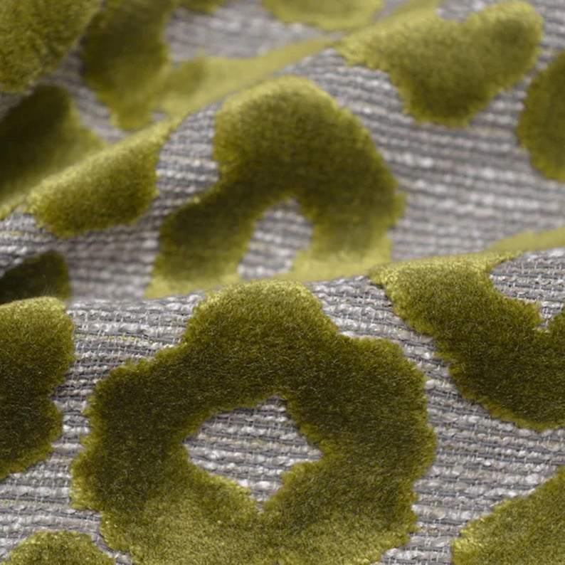 May include: A fabric featuring a raised, olive green velvet floral pattern set against a textured, light gray woven background. The material displays a distinct contrast between the soft, plush velvet shapes and the coarse, grid-like weave of the base.