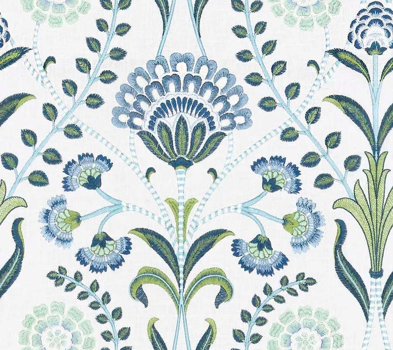 May include: A white fabric featuring an intricate embroidered floral pattern in shades of navy blue, light blue, and lime green. The design consists of symmetrical botanical motifs, including large central blossoms and leafy vines.