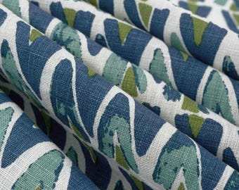 May include: A folded piece of fabric featuring a repeating geometric pattern in shades of navy blue, teal, and olive green on a white background. The textile has a visible woven texture and is arranged in soft, cascading folds across the frame.