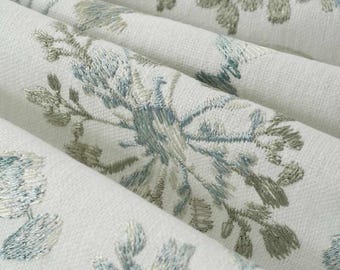 May include: Off-white fabric featuring an intricate embroidered floral pattern in shades of sage green and dusty blue. The textile displays a textured weave with repeating botanical motifs arranged in a series of soft, cascading folds.