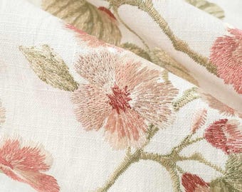 May include: A white fabric featuring an embroidered floral pattern with soft pink petals, deep red centers, and muted olive green leaves and stems. The embroidery has a textured, thread-based finish across the surface of the material.