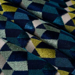 Puede incluir: Primer plano de una tela texturizada con un patr&oacute;n geom&eacute;trico. El dise&ntilde;o presenta formas de diamantes en tonos de azul, verde azulado, verde, amarillo y beige. La tela parece estar doblada, creando sombras y profundidad.