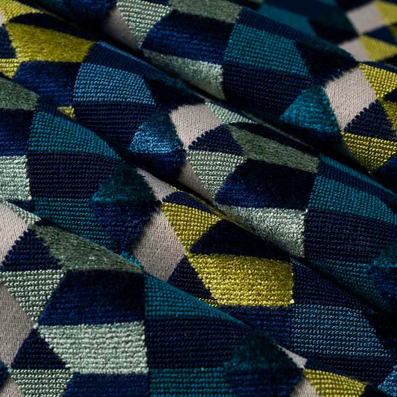 Puede incluir: Primer plano de una tela texturizada con un patr&oacute;n geom&eacute;trico. El dise&ntilde;o presenta formas de diamantes en tonos de azul, verde azulado, verde, amarillo y beige. La tela parece estar doblada, creando sombras y profundidad.