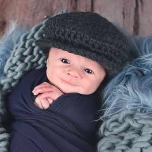May include: A newborn baby wearing a dark gray knitted cap, wrapped in a dark blue swaddle, and lying in a blue knitted basket.