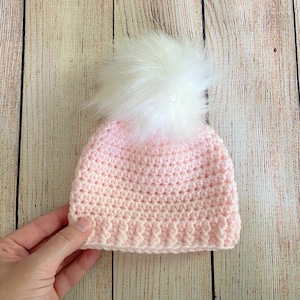 May include: A pink crocheted hat with a white faux fur pom pom.