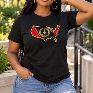 May include: A black short-sleeved t-shirt featuring a graphic of the United States map outlined in gold. The map interior displays a red and black color scheme with a central gold emblem consisting of a staff surrounded by a circular wreath design.