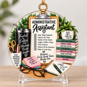 May include: A round acrylic ornament featuring a clipboard labeled Administrative Assistant with a checklist, a black tumbler with text, a stack of books, a potted plant, a pen holder, eyeglasses, and sticky notes with office-themed text.