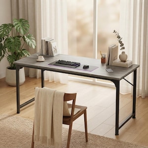 May include: A rectangular desk with a gray wood-grain surface and a black metal frame. The desk holds a black computer keyboard, a computer mouse, a mouse pad, books, a small cup, and a vase. A wooden chair with a beige throw blanket is positioned in front.