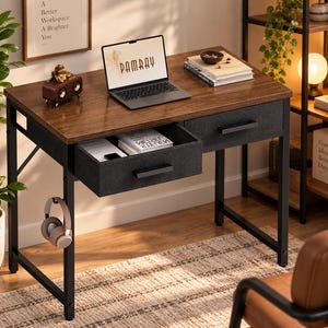 May include: A rectangular desk with a dark wood grain surface and a black metal frame. It features two fabric drawers with black handles, one of which is pulled open. A side hook holds a pair of headphones, and the desk surface supports a laptop.