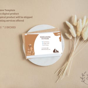 Puede incluir: Una tarjeta de visita rectangular de 3,5 por 2 pulgadas con un diseño en tonos marrón y blanco. La tarjeta muestra el texto Paws & Paths Dog Walker, un gráfico de dos perros e iconos para paseo de perros, visitas a cachorros y cuidado.