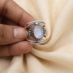 Peut inclure: Une bague en argent avec une pierre de lune ovale en cabochon sertie dans une bordure en corde torsadée avec des perles métalliques décoratives. L'anneau se compose de deux fils d'argent parallèles reliés au sertissage central. Texte jaipursilverbazar.