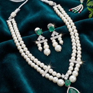Peut inclure: Un collier de perles à double rang orné d'un pendentif en pierre verte en forme de goutte, agrémenté de cristaux clairs et d'entretoises en métal argenté. L'ensemble comprend des boucles d'oreilles assorties avec une pierre verte ronde.