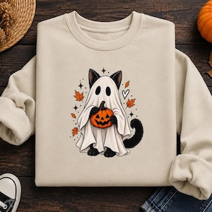 Puede incluir: Una sudadera beige de cuello redondo con un gráfico de un gato negro vestido con un disfraz de fantasma blanco. El gato sostiene una pequeña calabaza naranja. El diseño incluye hojas de otoño naranjas, pequeñas estrellas negras y un corazón blanco.