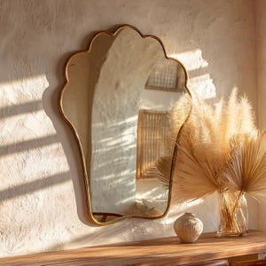 May include: A wall-mounted mirror with a scalloped, shell-like gold frame. The reflective surface shows a distorted view of a room with textured walls and light streaming through blinds, creating a pattern of horizontal shadows across the wall.