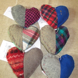 May include: Six handmade felt heart ornaments, each with a different patterned fabric. The hearts are sewn together with a contrasting thread and have a safety pin attached.