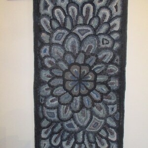 May include: A hand-hooked rug with a blue and gray floral design. The rug is made of wool and has a fringed edge.