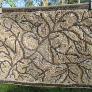 May include: A hand-hooked rug with a brown and beige floral design. The rug is made of wool and has a fringed edge.
