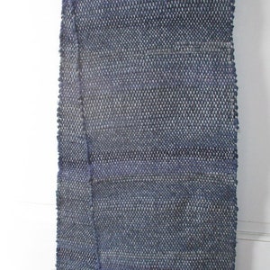 May include: A handwoven wool scarf in a deep blue color with a subtle white fleck throughout. The scarf has a fringe on both ends.