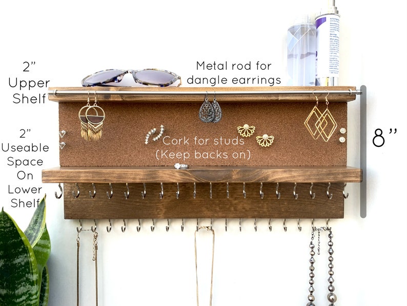 May include: A wooden jewelry organizer with two shelves. The top shelf has a corkboard for stud earrings and a metal rod for dangle earrings. The bottom shelf has hooks for necklaces. The organizer is 8 inches tall and the shelves are 2 inches deep.