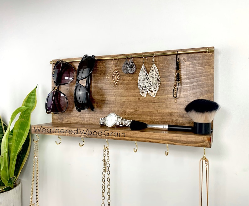May include: A wooden wall-mounted organiser with a shelf and hooks for jewellery, sunglasses, and other accessories. The organiser has a weathered wood grain finish and the text "Weathered Wood Grain" is printed on the shelf.