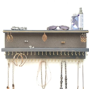 May include: A gray wooden jewelry organizer with gold hooks and a gray felt-lined top shelf. The organizer has a row of hooks for necklaces and a top shelf for earrings and other small jewelry.