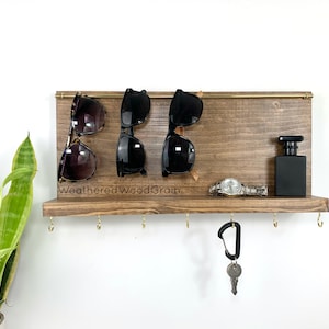 May include: A wooden wall-mounted organiser with hooks for keys and a shelf for sunglasses, a watch, and a small bottle. The shelf is stained a dark brown and has the text "WeatheredWoodGrain" printed on it.