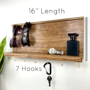May include: Wooden wall organiser with a shelf, 7 hooks, and a gold bar for hanging sunglasses. It measures 16 inches long and 7.5 inches high. The text "WeatheredWoodGrain" is printed on the shelf.