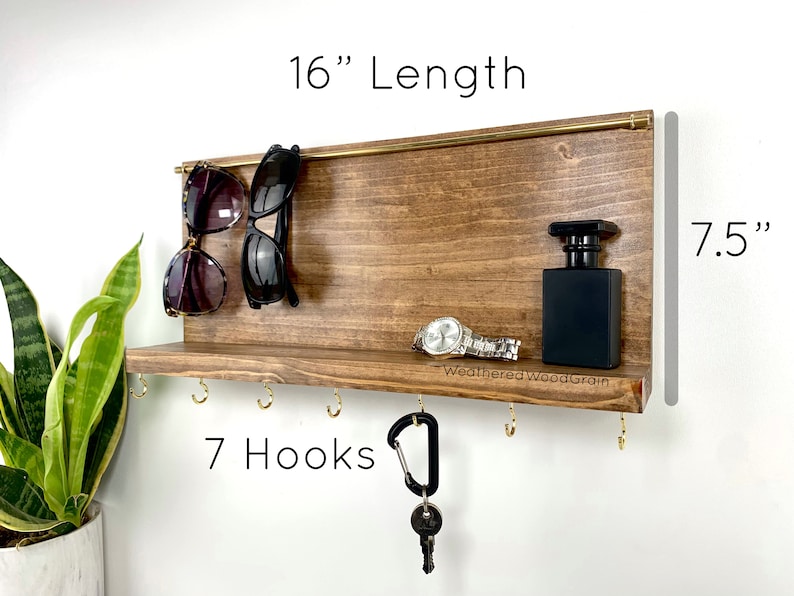 May include: Wooden wall organiser with a shelf, 7 hooks, and a gold bar for hanging sunglasses. It measures 16 inches long and 7.5 inches high. The text "WeatheredWoodGrain" is printed on the shelf.