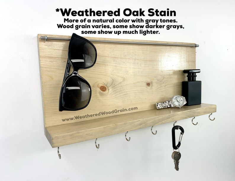 May include: A weathered oak wood key holder with a shelf and hooks. The shelf has a watch, a bottle of perfume, and sunglasses on it. The text "*Weathered Oak Stain" is at the top of the key holder. The text "More of a natural colour with grey tones. Wood grain varies, some show darker greys, some show up much lighter." is below the title. The text "www.WeatheredWoodGrain.com" is at the bottom of the key holder.