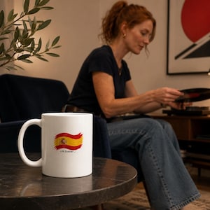 Puede incluir: Una taza de cerámica blanca con un gráfico de la bandera de España en estilo de pincelada y el texto "I'm forever..." impreso debajo. La taza tiene una forma cilíndrica estándar con un asa curva en el lado izquierdo sobre un fondo neutro.