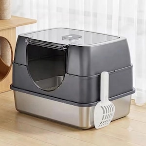 May include: A rectangular cat litter box featuring a metallic silver stainless steel base and a dark gray plastic top cover with a clear front entry door. A white plastic slotted scoop is attached to the side of the litter box unit.