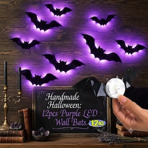 May include: A set of 12 black bat-shaped wall decorations featuring purple LED lights. Each bat includes a circular battery-operated light component on the back. A chalkboard sign displays the text: Handmade Halloween: 12pcs Purple LED Wall Bats.