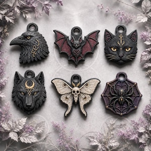 Op de afbeelding: Zes decoratieve hangers met gedetailleerde dier- en insectmotieven: een zwarte raaf, een vleermuis met rode vleugels, een zwarte kat, een wolf met een maansikkel, een crèmekleurige nachtvlinder met een schedel en een zwarte spin op een web.