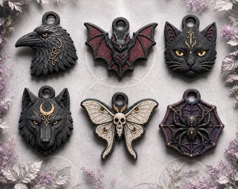Puede incluir: Seis colgantes decorativos con motivos detallados de animales e insectos: un cuervo negro, un murciélago de alas rojas, un gato negro, un lobo con una luna creciente, una polilla color crema con una calavera y una araña negra en una telaraña.