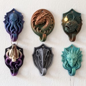 May include: A set of six wall-mounted decorative hooks featuring sculpted designs including an octopus, a dragon, an anglerfish with a light, a skull with tentacles, a bird skull, and a mermaid face, each mounted on a shield or circular base.