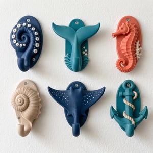 May include: A set of six nautical-themed wall hooks featuring an octopus tentacle, a whale tail, a seahorse, a seashell, a stingray, and an anchor. Each hook is mounted on an oval base with visible screws, showcasing distinct marine shapes.