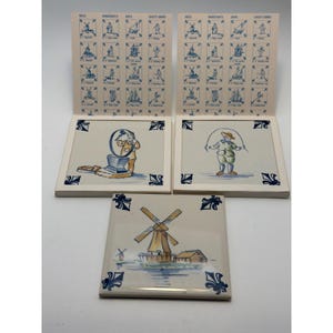 May include: Three square ceramic tiles featuring blue and yellow hand-painted illustrations. Two tiles are attached to cards with grids of small blue icons labeled Mills, Handicrafts, Ships, and Child's Games. One tile depicts a windmill.