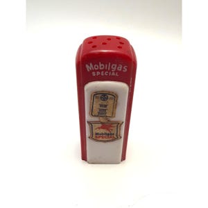 May include: A red and white plastic shaker shaped like a vintage petrol pump. The top features six holes for dispensing. The front displays the text Mobilgas SPECIAL in white, along with two rectangular labels featuring the Mobilgas logo and Pegasus.