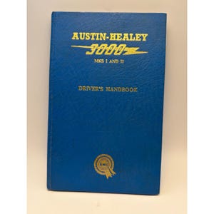 May include: A blue driver's handbook for the Austin-Healey 3000 Mks I and II. The cover features gold embossed text reading AUSTIN-HEALEY 3000 MKS I AND II and DRIVER'S HANDBOOK, with a circular BMC logo at the bottom centre of the textured blue cover.