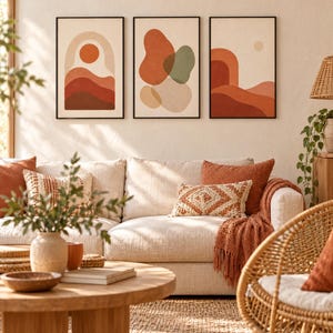 May include: A set of three framed wall art prints featuring abstract shapes and landscapes in shades of terracotta, sage green, and cream. The artwork is displayed in thin black frames, showcasing layered hills, a sun, and organic blobs.