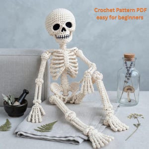 Puede incluir: Una figura de esqueleto tejida a ganchillo en color crema con cuencas oculares negras y dientes bordados. El texto "Crochet Pattern PDF easy for beginners" es visible en la esquina superior derecha. El esqueleto tiene puntos visibles.