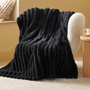 May include: A plush black throw blanket featuring a deep, vertical ribbed texture. The fabric has a soft, fuzzy appearance with distinct raised channels running from top to bottom, creating a consistent pattern across the entire surface of the item.