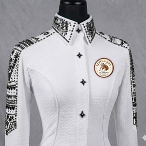 May include: A white long-sleeve shirt with a textured fabric, featuring a pointed collar and shoulders heavily embellished with dark metallic studs and crystals. A circular patch on the chest displays the text Stitch & Sole Clothing.